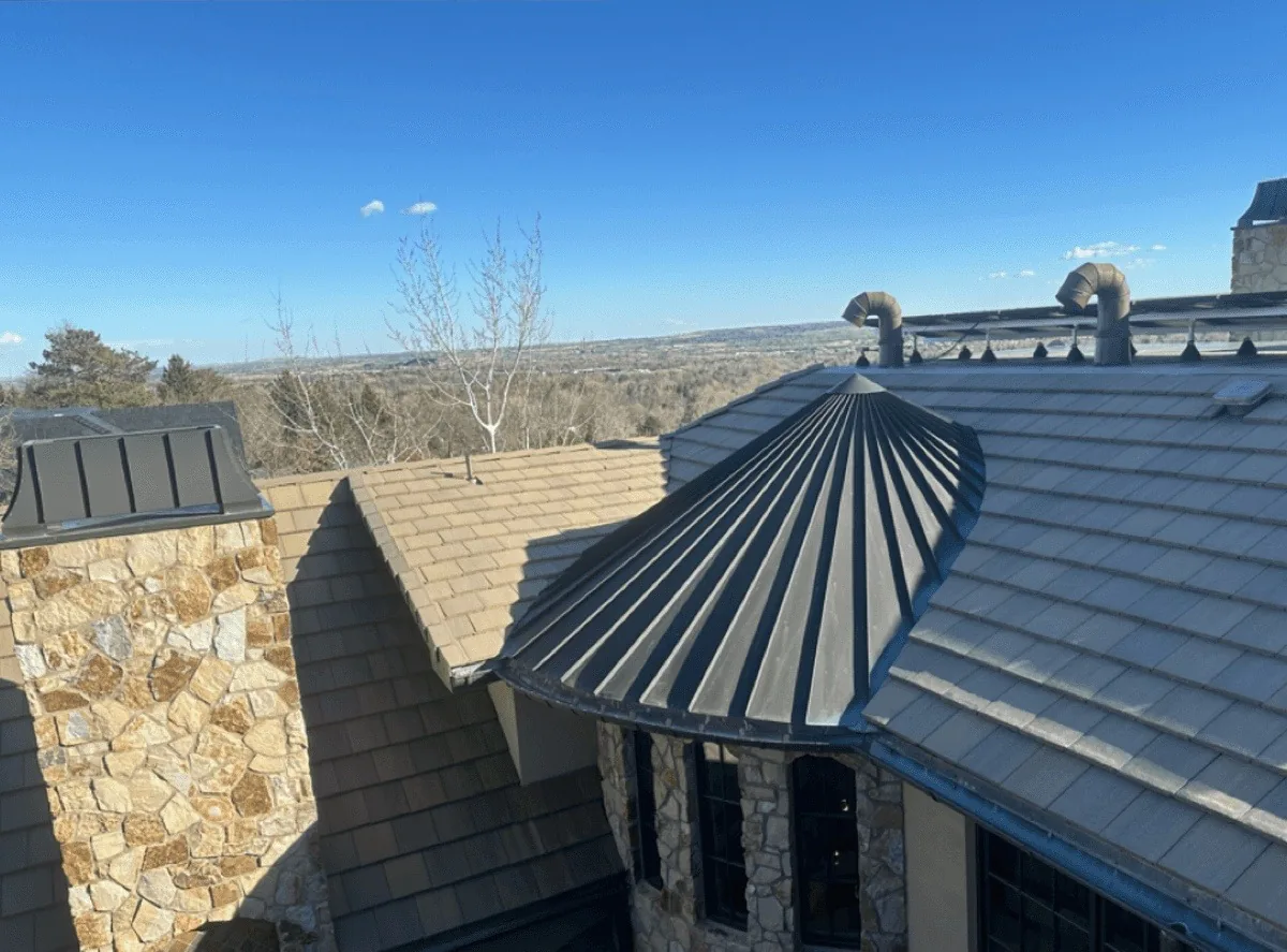 Standing-seam metal turret roof over concrete tile on a Front Range home, with the plains visible beyond